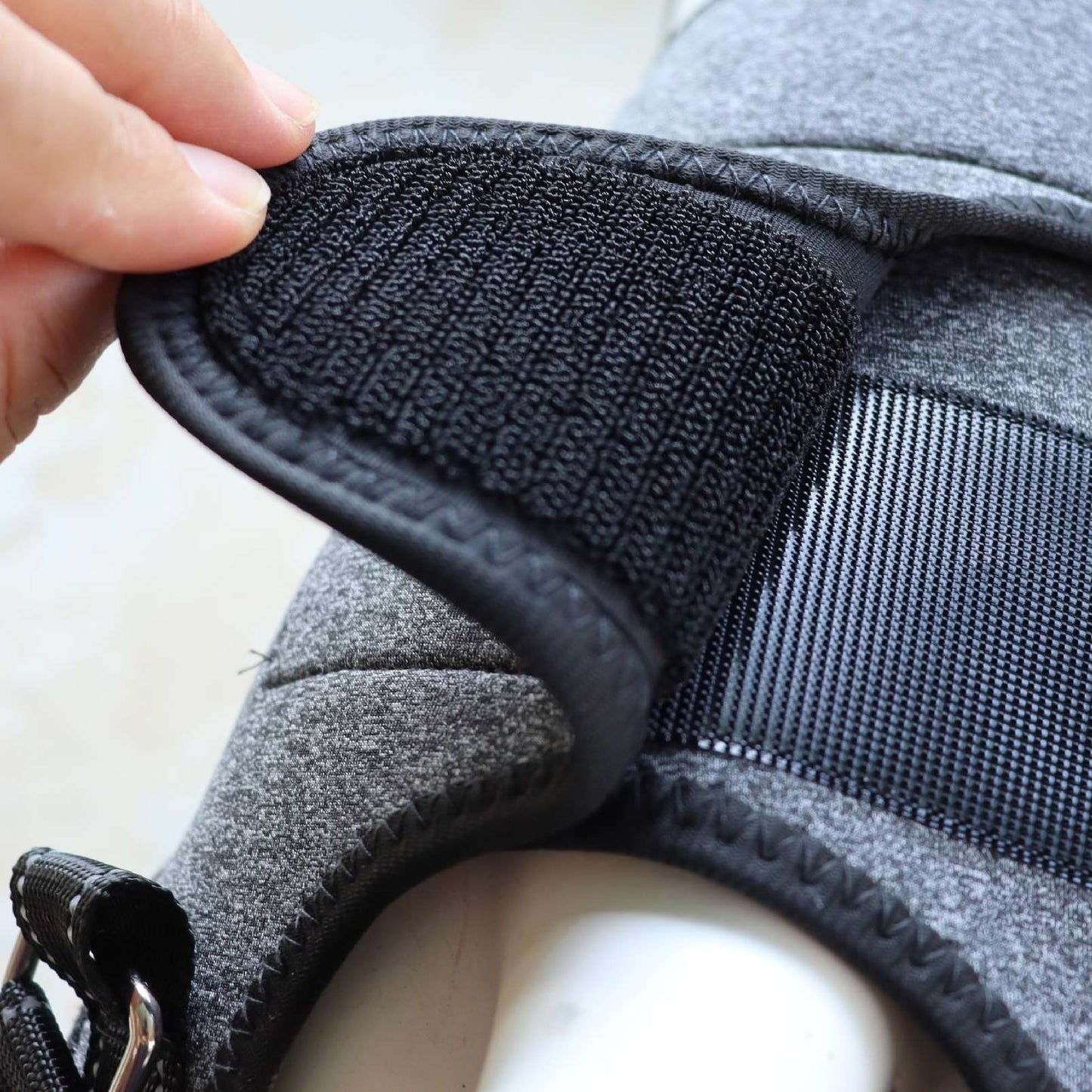 Close-up of a gray pet Full-Body Split Lifting Support harness with a hand adjusting a black strap.